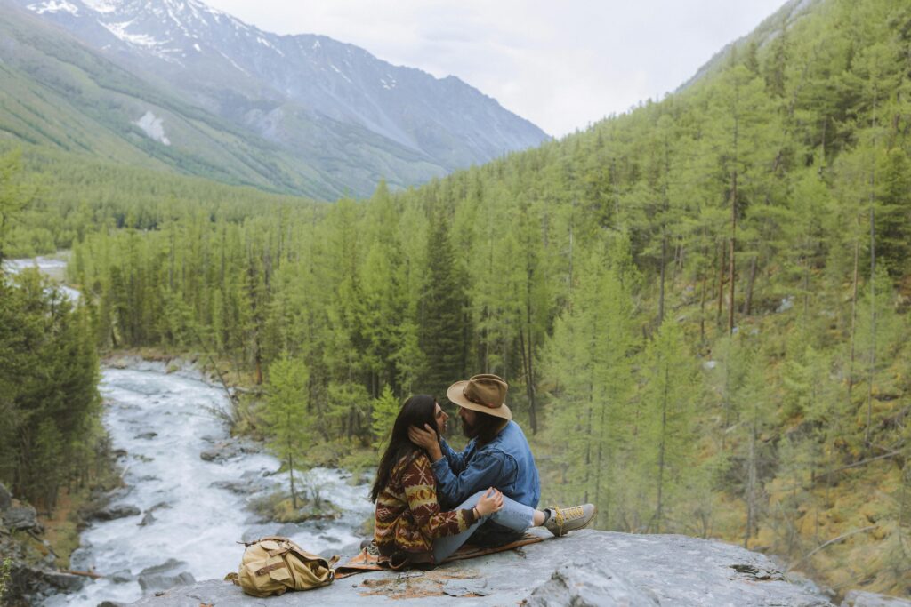 Couple embracing on a rock with a scenic mountain and forest backdrop, capturing love in nature.